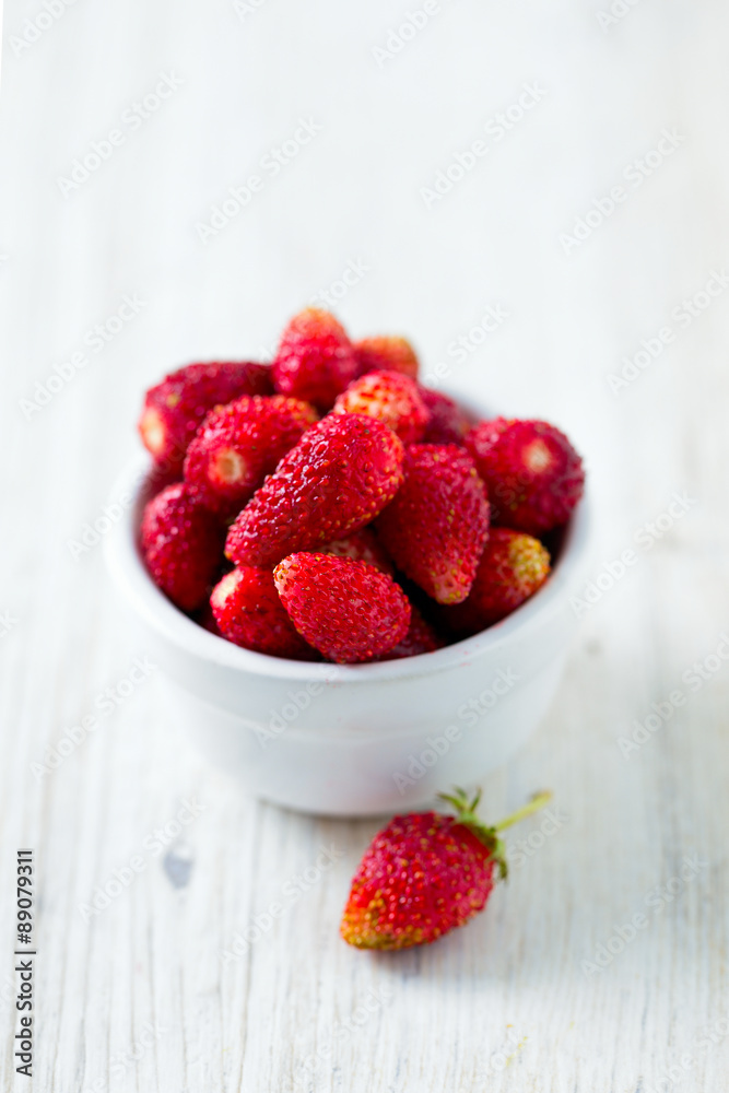 wild strawberries in a bowl on wooden surface wild strawberries in a bowl on wooden surface