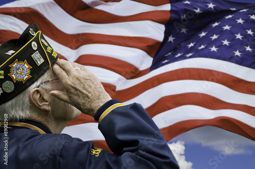 A veteran is saluting in front of US flag.