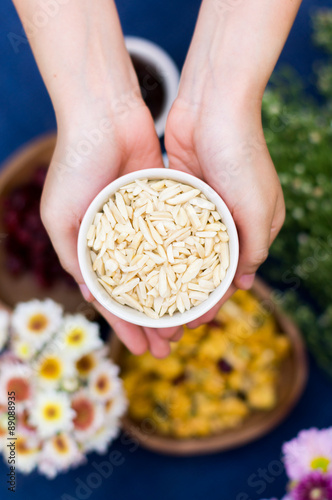 Hands hold almond shredded seeds in white bowl
