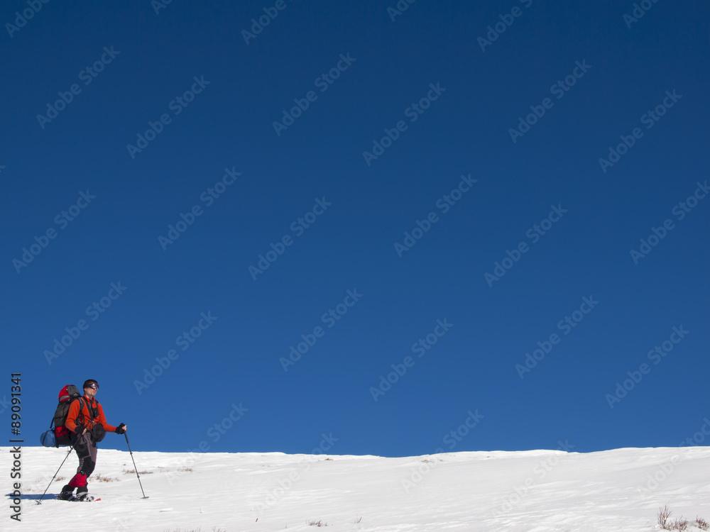 A man in snowshoes walks in the mountains with a backpack.