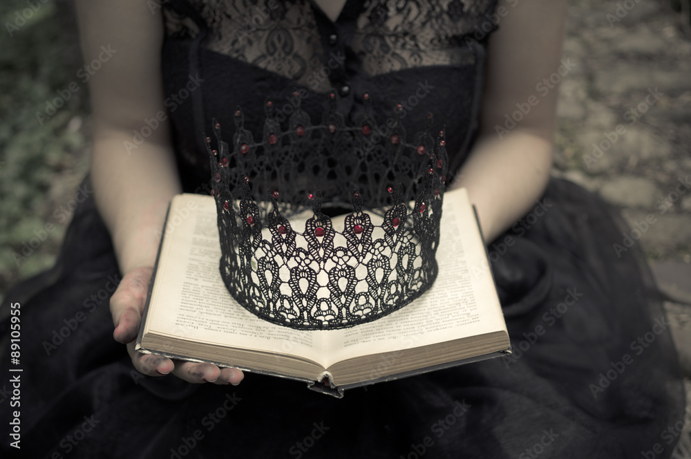 Woman in black dress holdings a book and crown