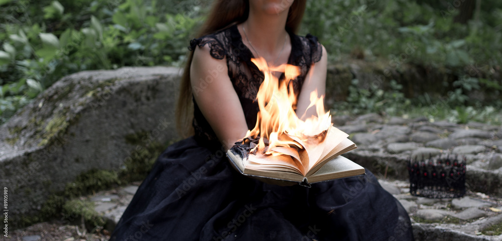 A sitting woman in a black dress holds black burning book