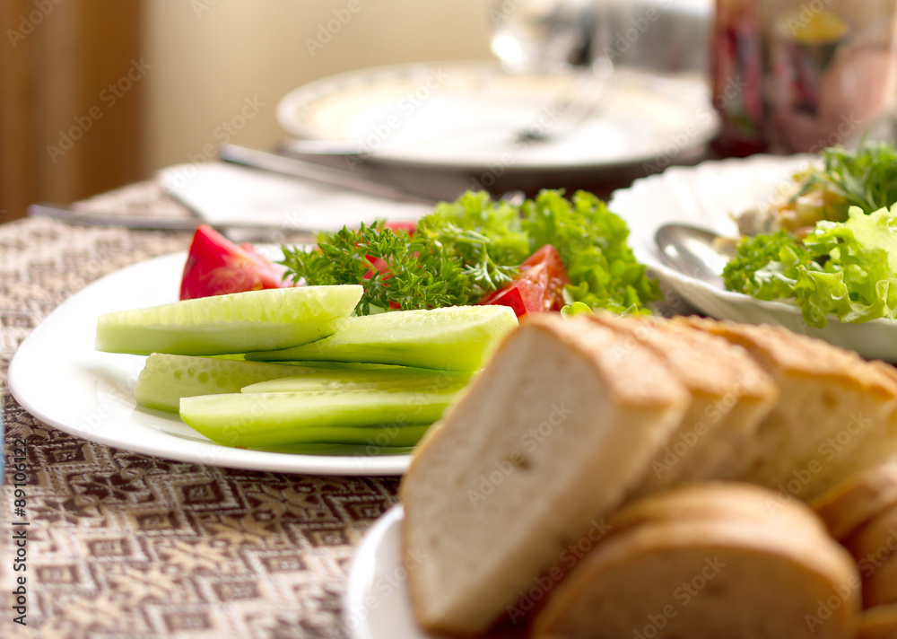 Bread and various salads of tomatoes, cucumbers on white plates on a table in a restaurant