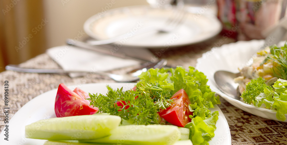 Lettuce, tomato, cucumber on a white plate on a table in a restaurant