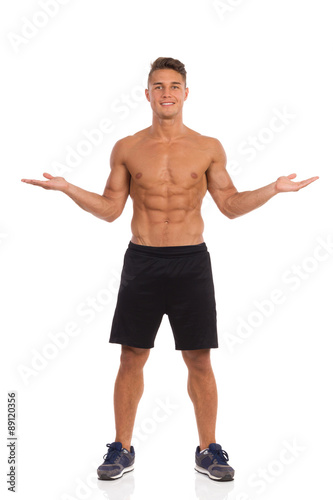 The Choice. Young muscular man in black shorts posing with arms outstretched. Front view. Full length studio shot isolated on white.
