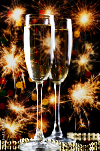 Two glasses of champagne on bright background with sparklers