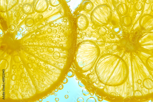 Fresh lemon slice in water with bubbles on sky background