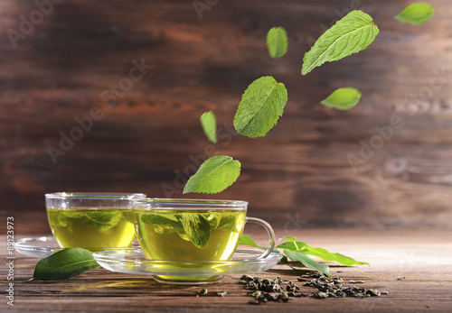 Mint leaves falling in cups of green tea on wooden background