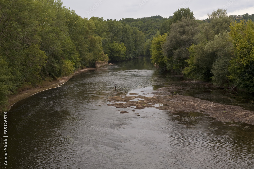 La Vezere River, France with the Full Moon. The waters run calm and peaceful early in the morning in summer. A sole man stands in the shallows fishing. La Vezere River, France with the Full Moon. The waters run calm and peaceful early in the morning in summer. A sole man stands in the shallows fishing.