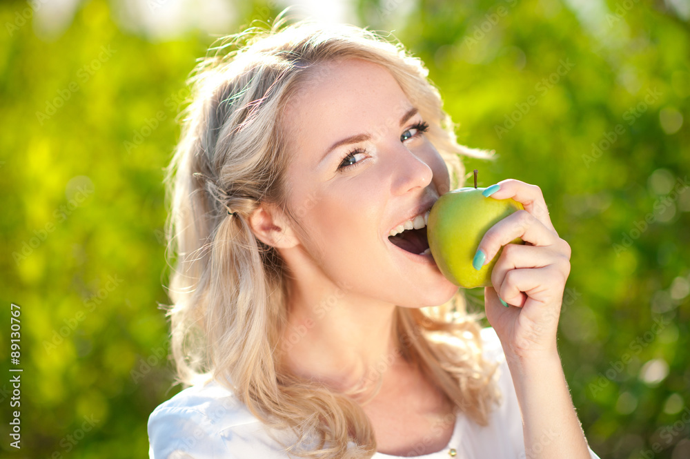 Smiling blonde girl biting green apple outdoors. Looking at camera. Healthy eating. Smiling blonde girl biting green apple outdoors. Looking at camera. Healthy eating.