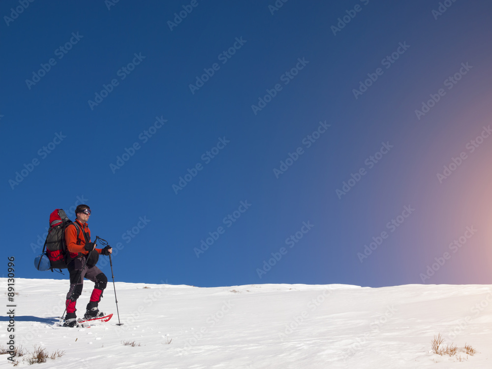 A man in snowshoes walks in the mountains with a backpack.