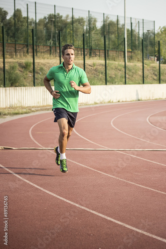 Musular blond runner running on tartan red sprint track, alone.