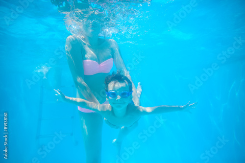 Young mother and toddler son swimming underwater in pool and having fun