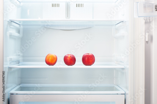 Three two-colored orange and red peaches on shelf of open empty refrigerator. Weight loss diet concept.
