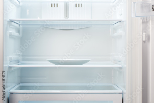 Empty white plate in open empty refrigerator. Weight loss diet concept.