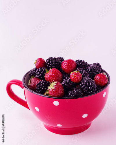 Blackberries and strawberries in a red plate. Isolated backgroun