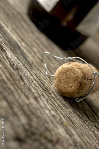 Champagne cork with attached wire lying on a rustic wooden table alongside a champagne bottle viewed at a very oblique tilted angle with copyspace.