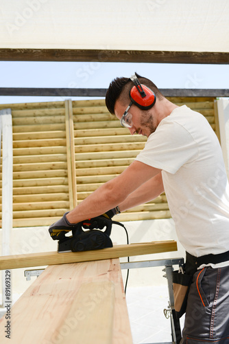 handsome young man carpenter working with electric tool on wood timber in construction site