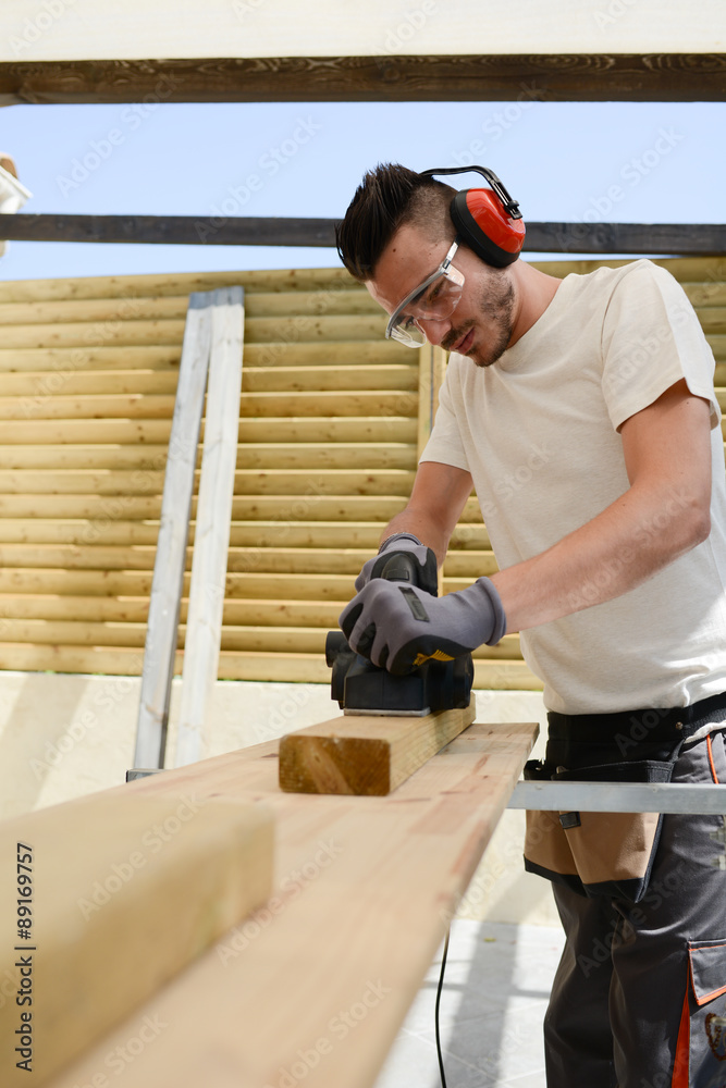 handsome young man carpenter working with electric tool on wood timber in construction site