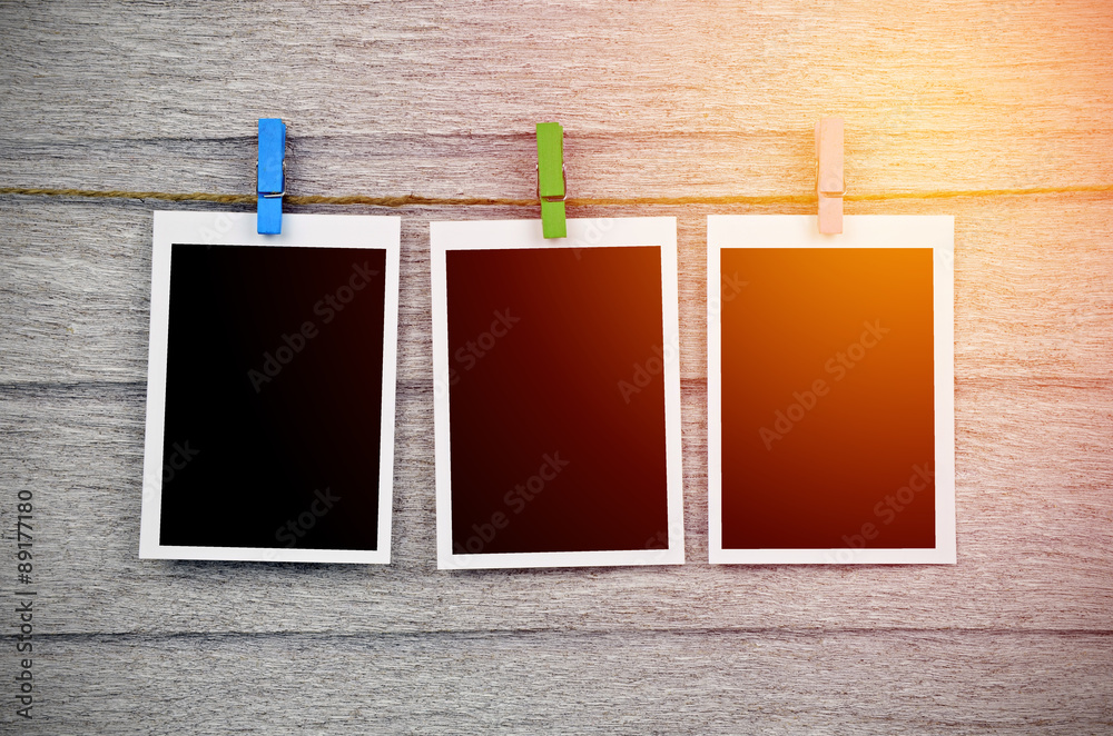 Fototapeta premium empty black photo frames hanging with clothespins on wooden back