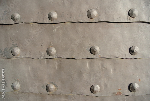Old grey iron surface with rivets; rough, rusty texture; iron gate.