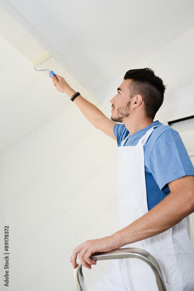 handsome young man professional painter applying white paint in wall with roller