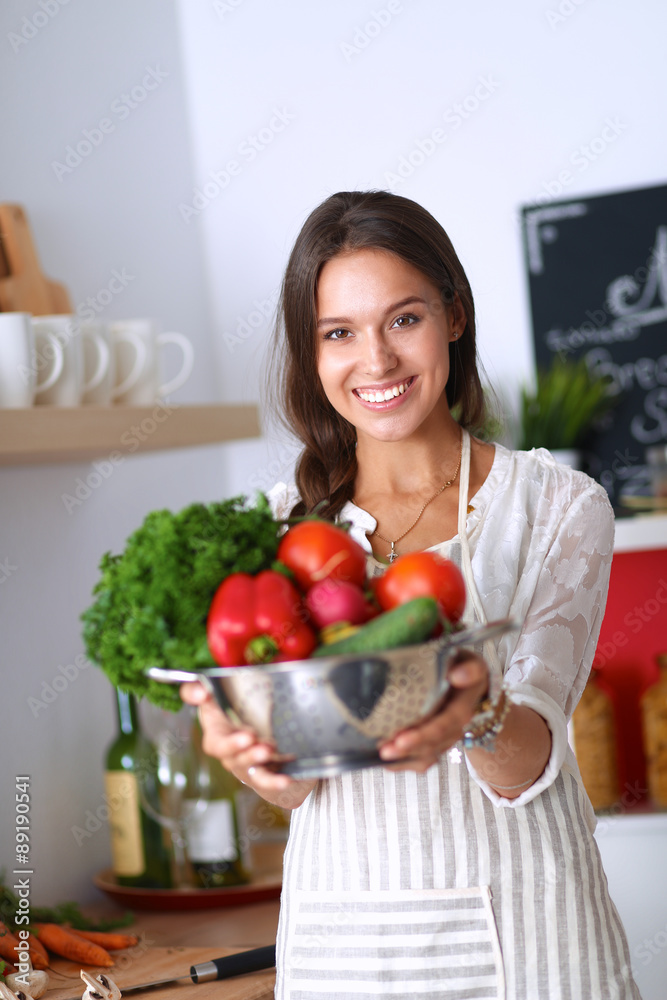 Smiling young woman holding vegetables standing in kitchen Smiling young woman holding vegetables standing in kitchen