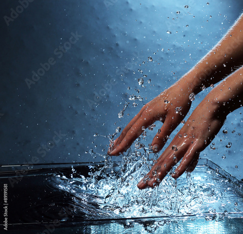 Female hands with water splashing on blue background