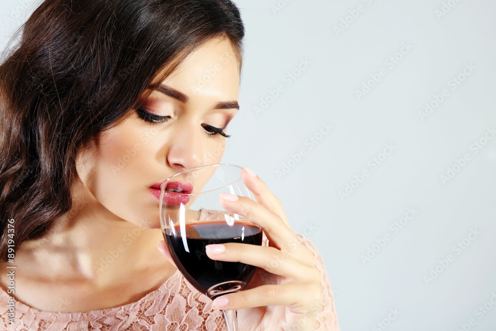 Portrait of young woman with glass of red wine on grey background Portrait of young woman with glass of red wine on grey background