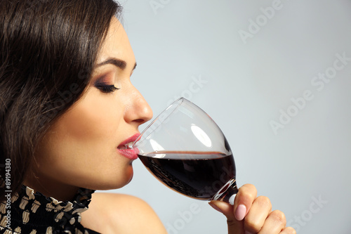 Portrait of young woman with glass of red wine on grey background