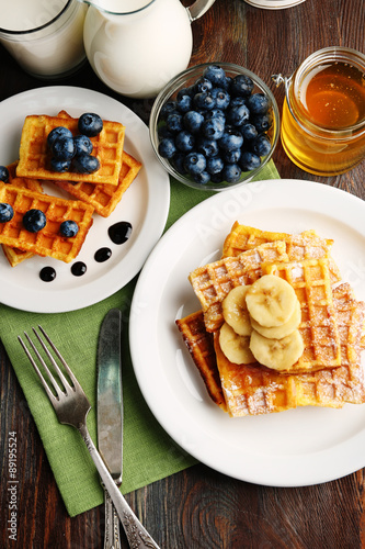 Sweet homemade waffles with sliced banana on plate, on light background