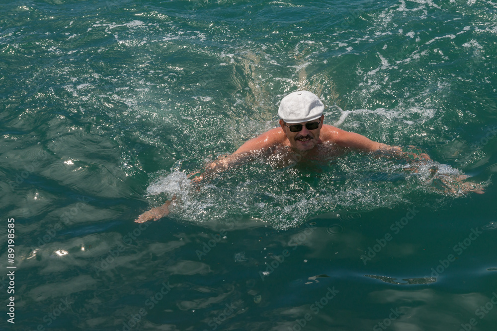Mature man is swimming in blue-green sea water.