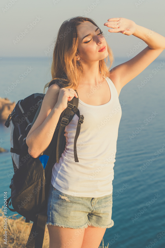 Happy backpacker girl is standing on rock over ocean view Happy backpacker girl is standing on rock over ocean view