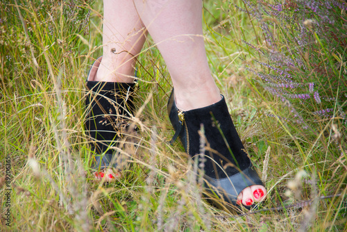 Shoes in grass. Legs of a young woman wearing high heels, in grass with heather to the sides.