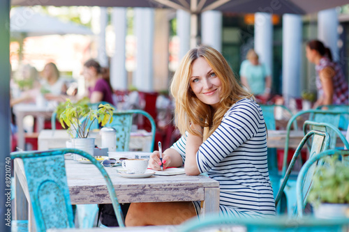 Woman drinking coffee and writing notes in cafe