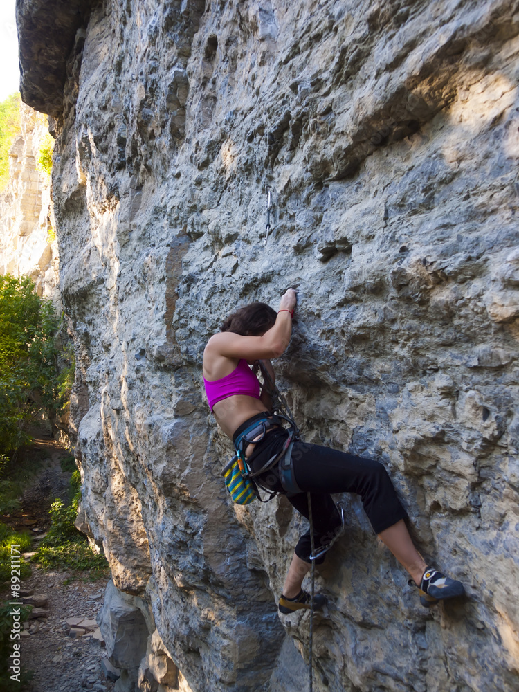 Young woman with rope climbs on the rock.