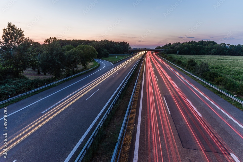 german highway at sunset with light trails from passing cars