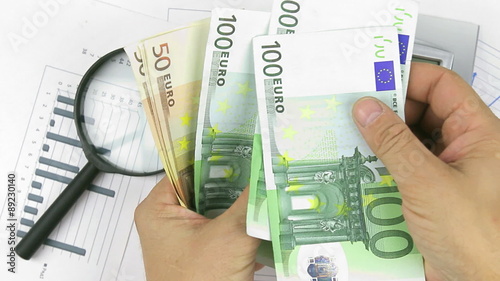 Businessman believes euros and throws them at documents, 
calculator, magnifying glass