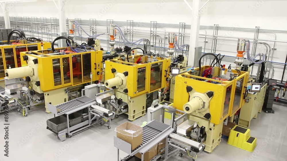 Tracking along a factory floor from a high angle, showing multiple large injection mold machines. 
