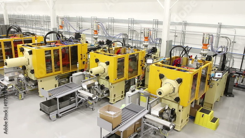 Tracking along a factory floor from a high angle, showing multiple large injection mold machines. 
