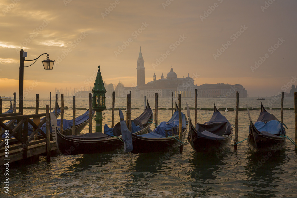 Gondolas by Saint Mark square during sunrise with San Giorgio di Maggiore church in the background in Venice Italy