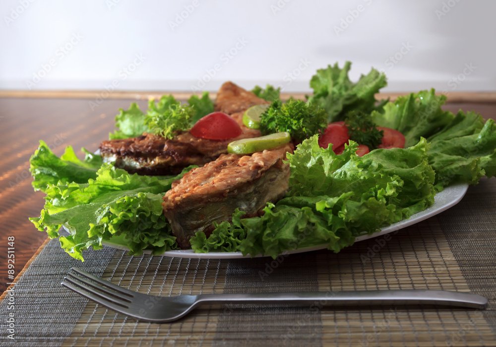 A piece of fried fish fillett served on blue glass table with lettuce, lime, tomato and herbs A piece of fried fish fillett served on blue glass table with lettuce, lime, tomato and herbs