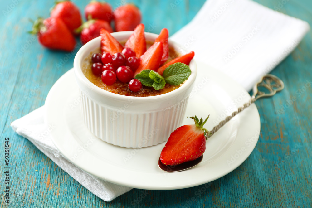 Creme brulee dessert with fresh strawberries and mint leaves, on color wooden background Creme brulee dessert with fresh strawberries and mint leaves, on color wooden background