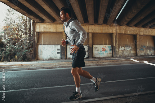 Jogger running in city environment.He wearing headphones around neck. © BalanceFormCreative