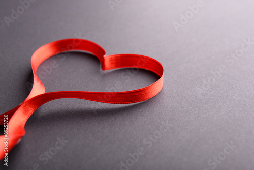 Red ribbon in shape of heart on gray background