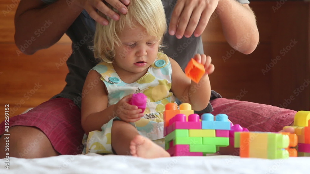 little girl plays with toy constructor father brushes her hair
