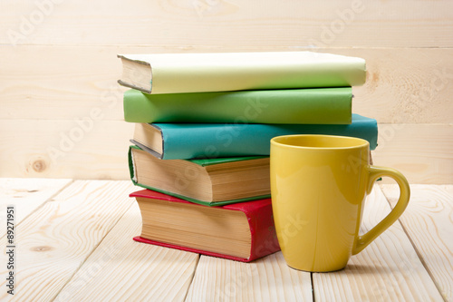 Stack of colorful books and cup on wooden table. Back to school. Copy space