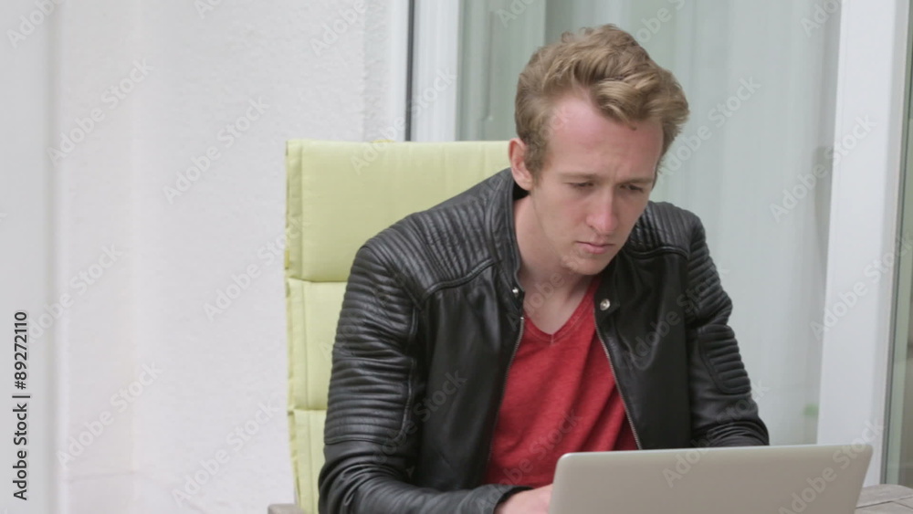 young blond man sitting outside on balcony and typing on laptop
young blond man sitting outside on balcony and typing on laptop