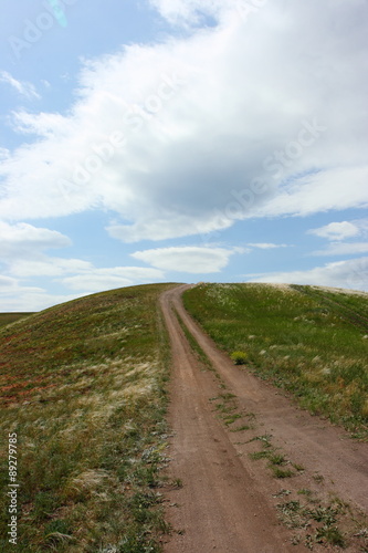 Steppe dirt road towards a hill top against a blue sky