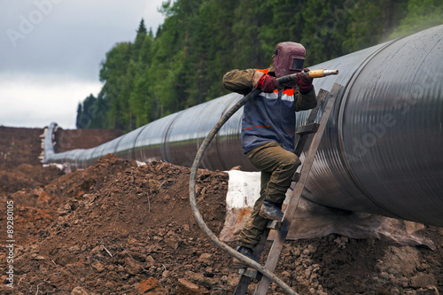 Worker using a sandblaster cleans tubing pipe before insulation photo